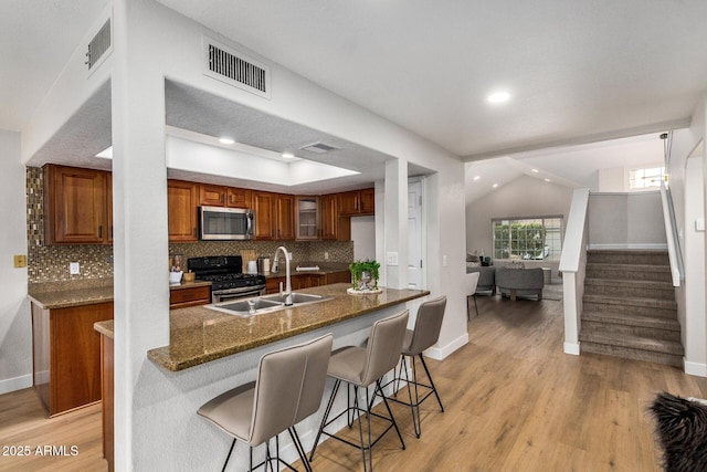 kitchen with sink, dark stone countertops, decorative backsplash, light hardwood / wood-style floors, and stainless steel appliances