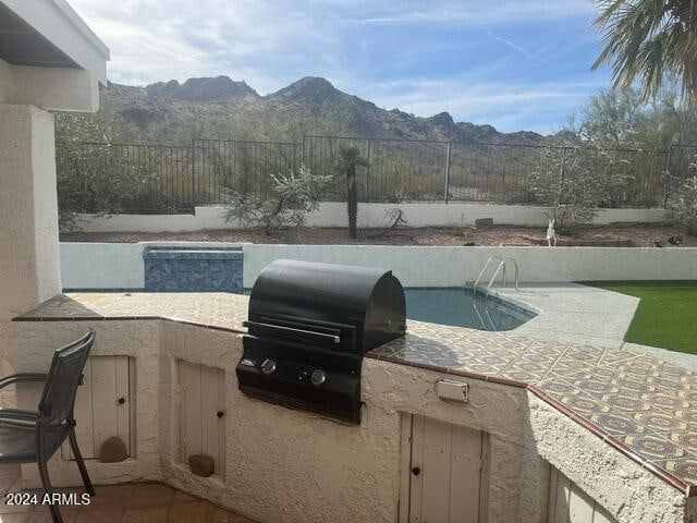 view of patio / terrace featuring a fenced in pool, grilling area, a mountain view, and an outdoor kitchen