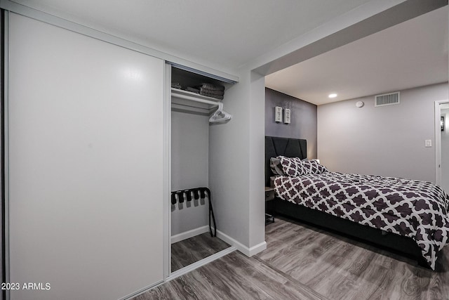 bedroom with baseboards, wood finished floors, visible vents, and a closet
