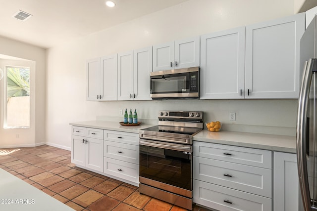 kitchen with stainless steel appliances, built in desk, white cabinets, and light tile patterned floors