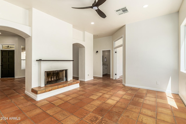 unfurnished living room with ceiling fan, a tiled fireplace, a healthy amount of sunlight, and tile patterned floors