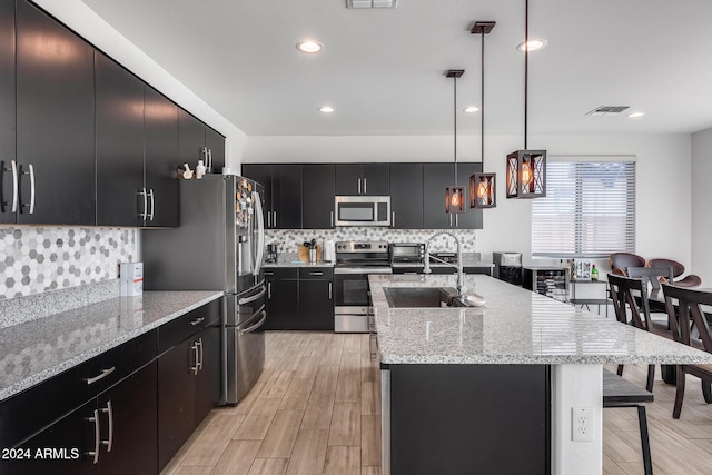 kitchen with sink, stainless steel appliances, an island with sink, pendant lighting, and light hardwood / wood-style floors