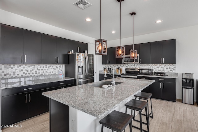 kitchen with sink, stainless steel appliances, hanging light fixtures, a kitchen breakfast bar, and a center island with sink