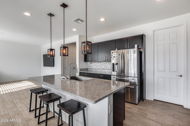 kitchen with light stone countertops, sink, hanging light fixtures, stainless steel refrigerator with ice dispenser, and light hardwood / wood-style floors