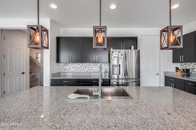 kitchen featuring light stone countertops, stainless steel refrigerator with ice dispenser, pendant lighting, and sink