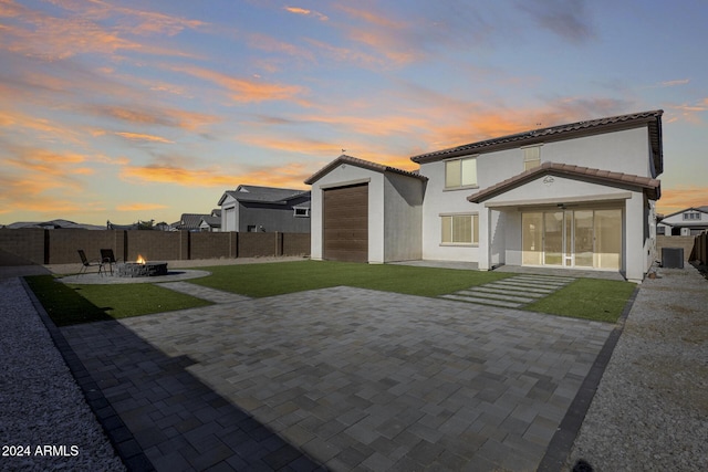 back house at dusk featuring central AC unit, an outdoor fire pit, a patio, a garage, and a lawn