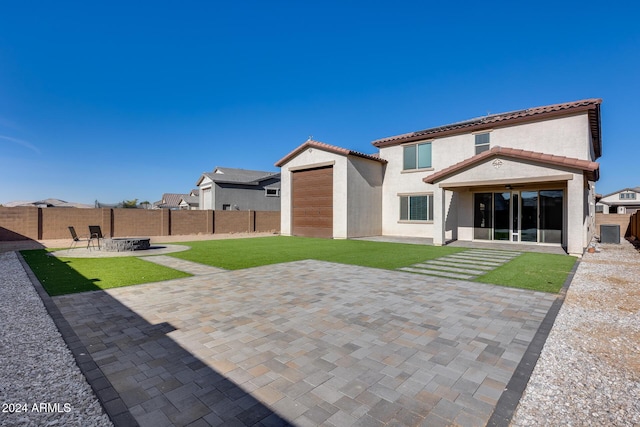 back of property featuring central AC, a fire pit, a patio area, a yard, and a garage