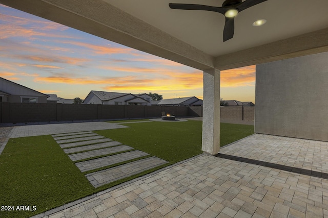 yard at dusk featuring ceiling fan and a patio