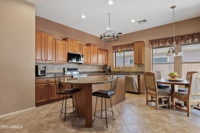 kitchen with visible vents, a kitchen island, appliances with stainless steel finishes, backsplash, and a notable chandelier