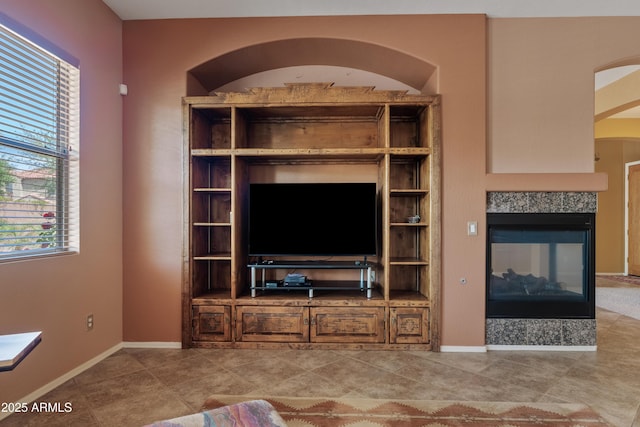 tiled living area with baseboards, arched walkways, and a multi sided fireplace