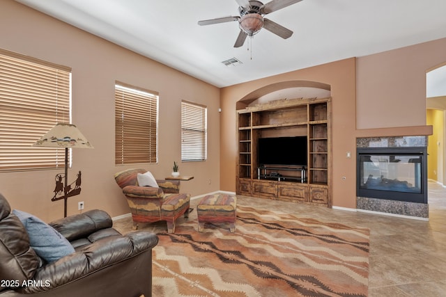 living area featuring built in features, a multi sided fireplace, a ceiling fan, baseboards, and visible vents
