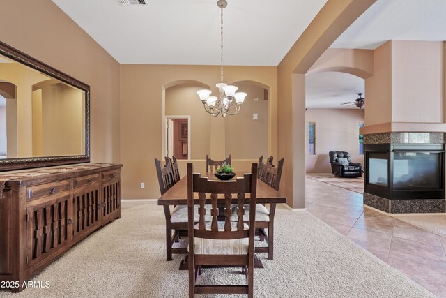 dining space featuring baseboards, arched walkways, a multi sided fireplace, and ceiling fan with notable chandelier
