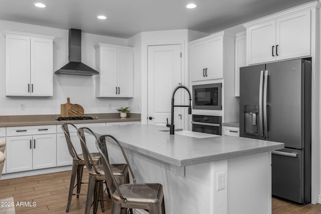 kitchen with black microwave, wall chimney range hood, stainless steel fridge with ice dispenser, light wood-style flooring, and white cabinets