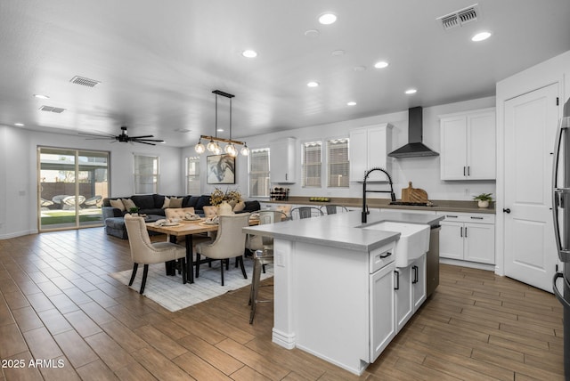 kitchen featuring wall chimney range hood, visible vents, and white cabinets