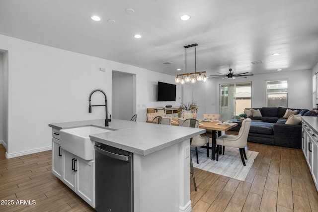 kitchen featuring dishwashing machine, wood finish floors, a kitchen island with sink, a sink, and open floor plan