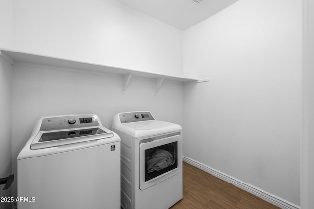 clothes washing area featuring washer and clothes dryer, laundry area, baseboards, and wood finished floors