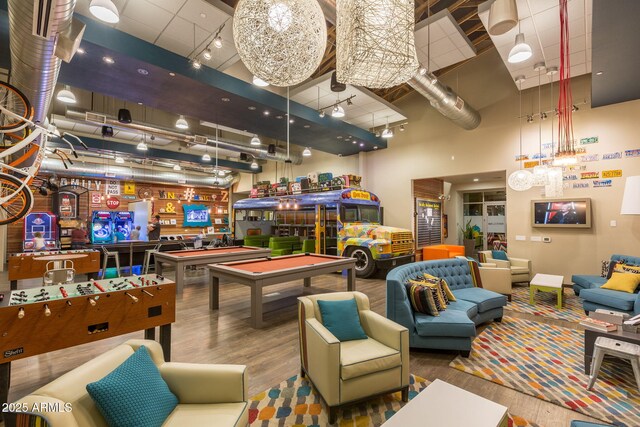 game room with billiards, rail lighting, wood finished floors, and a towering ceiling