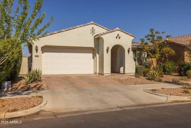 mediterranean / spanish-style house with stucco siding, a tiled roof, decorative driveway, and a garage