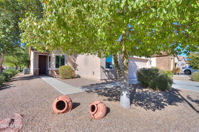 view of property hidden behind natural elements featuring central air condition unit and a garage