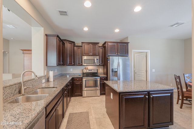 kitchen featuring light stone counters, dark brown cabinets, stainless steel appliances, sink, and a kitchen island