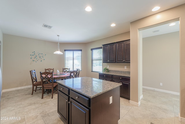 kitchen featuring decorative light fixtures, a kitchen island, light stone counters, and dark brown cabinetry