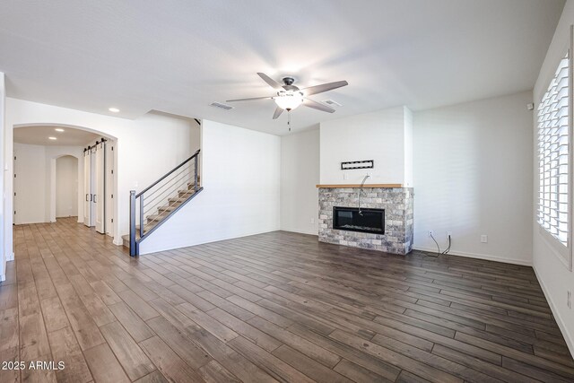 unfurnished living room with a barn door, dark wood-type flooring, and ceiling fan