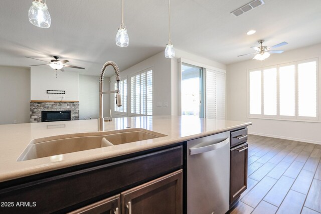 kitchen featuring a kitchen island with sink, dark wood-type flooring, hanging light fixtures, a fireplace, and ceiling fan