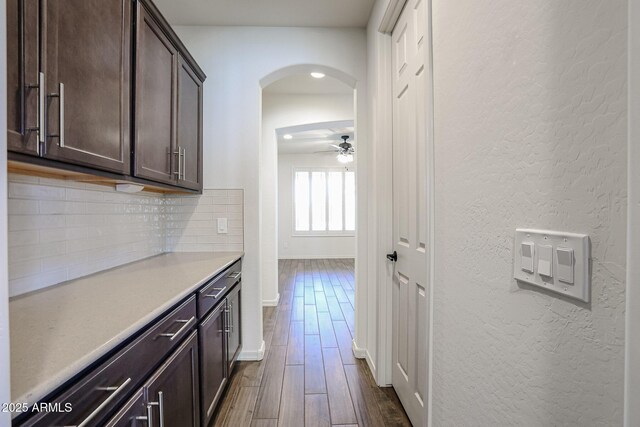 kitchen with tasteful backsplash, wall chimney range hood, stainless steel appliances, dark brown cabinetry, and dark hardwood / wood-style flooring