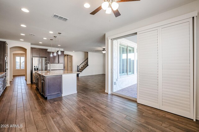 kitchen featuring pendant lighting, a center island with sink, wall chimney exhaust hood, and sink