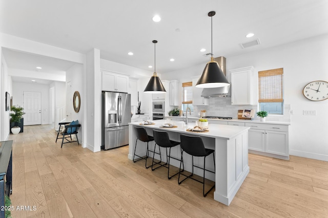 kitchen with hanging light fixtures, an island with sink, white cabinets, and appliances with stainless steel finishes