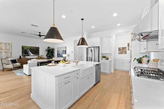 kitchen with ventilation hood, an island with sink, white cabinetry, sink, and stainless steel appliances