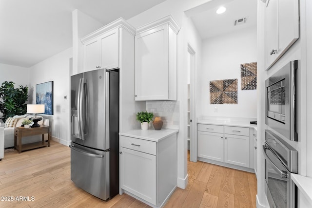 kitchen featuring white cabinetry, stainless steel appliances, backsplash, and light wood-type flooring