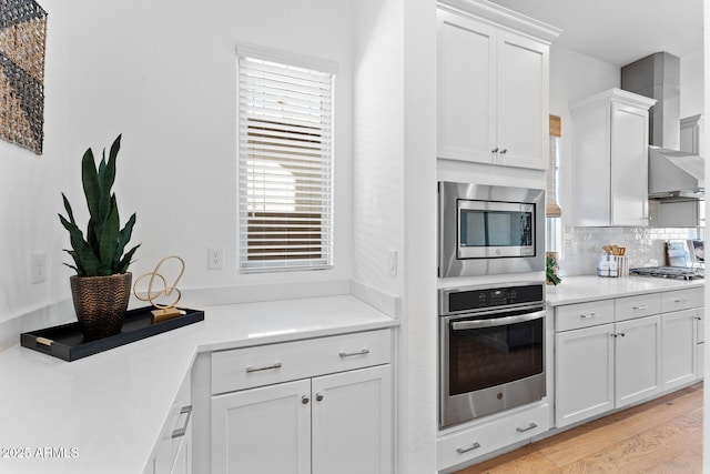 kitchen with white cabinetry, backsplash, stainless steel appliances, and light wood-type flooring