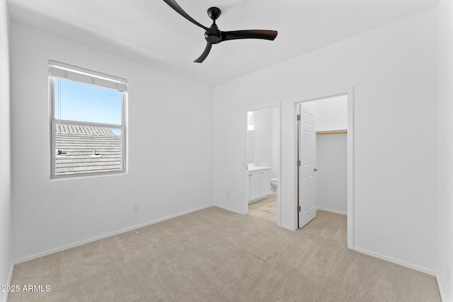 unfurnished bedroom with ensuite bath, ceiling fan, a spacious closet, light colored carpet, and a closet