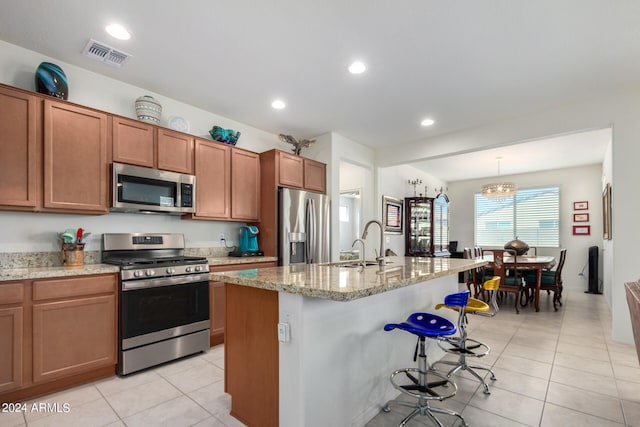 kitchen with decorative light fixtures, appliances with stainless steel finishes, a kitchen island with sink, sink, and light tile floors