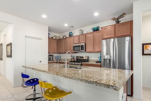 kitchen featuring a center island with sink, light tile floors, stainless steel appliances, and a breakfast bar area