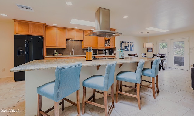 kitchen with a large island with sink, visible vents, black fridge, island range hood, and light tile patterned floors