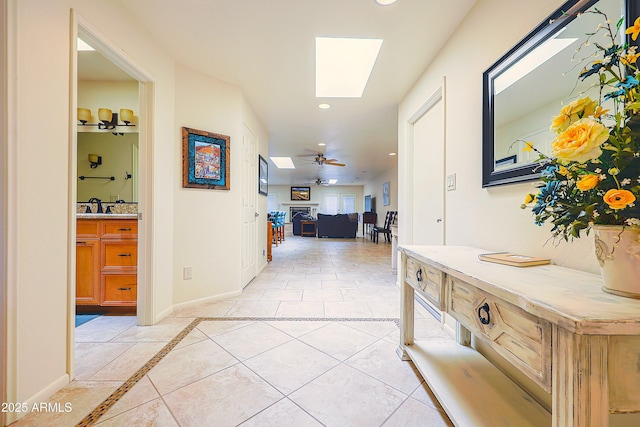 hallway featuring recessed lighting, light tile patterned floors, baseboards, a sink, and a skylight