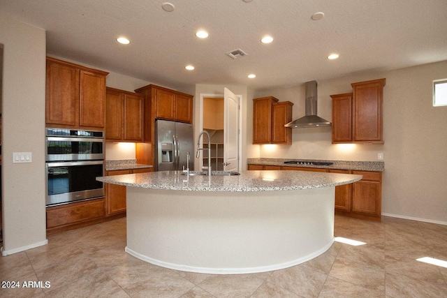 kitchen with a center island with sink, sink, appliances with stainless steel finishes, and wall chimney range hood