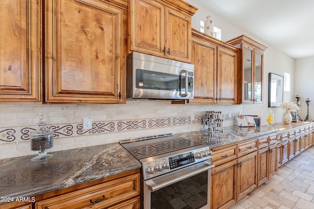 kitchen with appliances with stainless steel finishes, dark stone counters, and backsplash