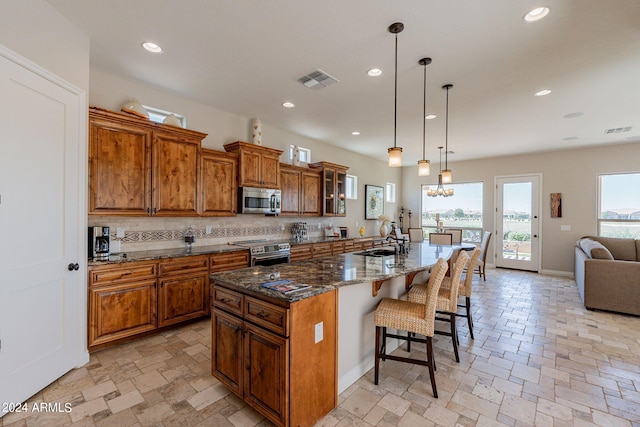 kitchen with appliances with stainless steel finishes, a wealth of natural light, backsplash, and a center island with sink