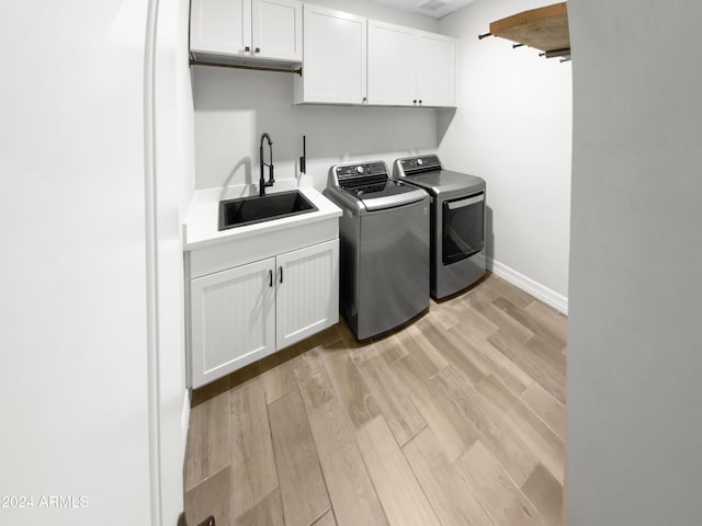 laundry room with washer and clothes dryer, light hardwood / wood-style floors, cabinets, and sink