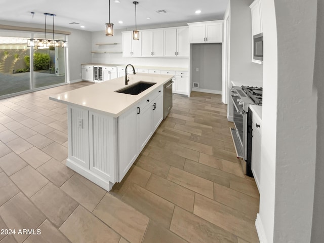 kitchen featuring a kitchen island with sink, white cabinets, hanging light fixtures, sink, and appliances with stainless steel finishes