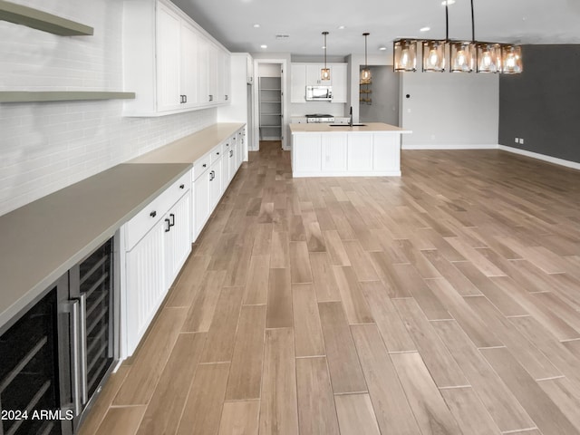 kitchen with a center island with sink, hanging light fixtures, decorative backsplash, light wood-type flooring, and white cabinetry