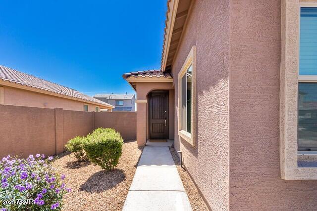 entrance to property featuring a tile roof, fence, and stucco siding