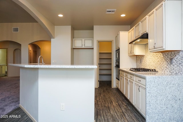 kitchen featuring under cabinet range hood, visible vents, decorative backsplash, black appliances, and a center island with sink