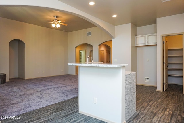 kitchen featuring arched walkways, a center island with sink, visible vents, a ceiling fan, and open floor plan