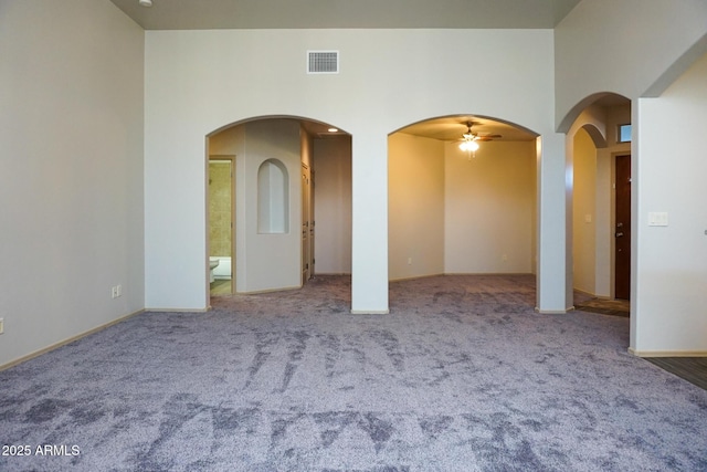 empty room with carpet, visible vents, a high ceiling, and arched walkways