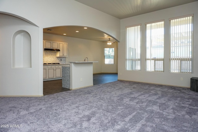 unfurnished living room with baseboards, arched walkways, a ceiling fan, dark colored carpet, and recessed lighting