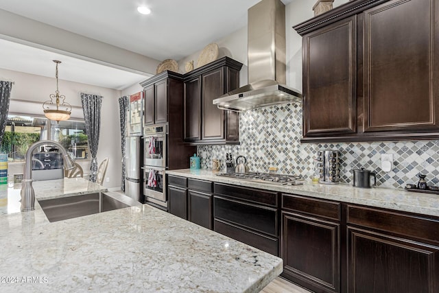 kitchen with light stone countertops, appliances with stainless steel finishes, decorative backsplash, wall chimney range hood, and sink